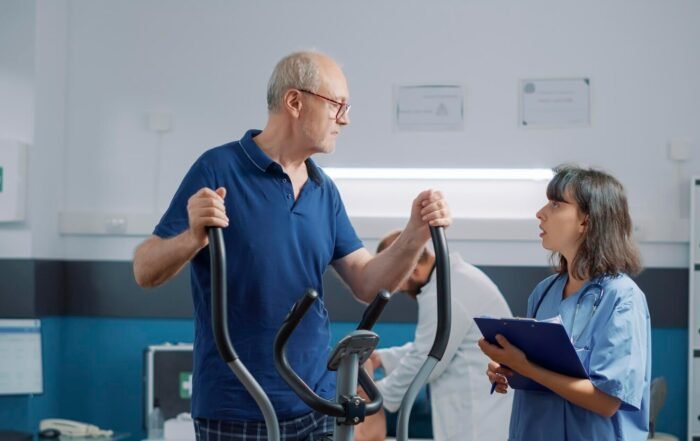 Senior Patient Doing Recovery Exercise Medical Cabinet Receiving Assistance From Rehabilitation Specialist Female Nurse Explaining Use Stationar Bicycle Physi